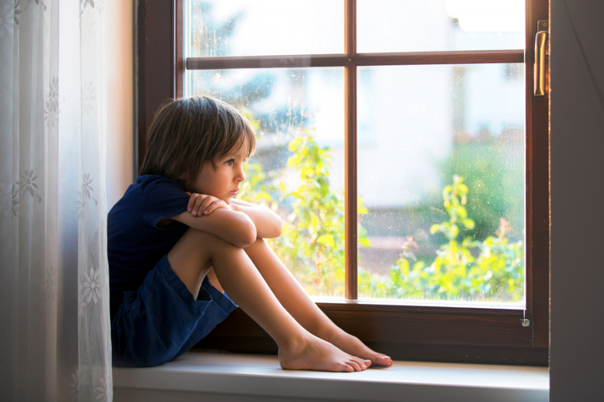 Sad child, boy, sitting in a window shield