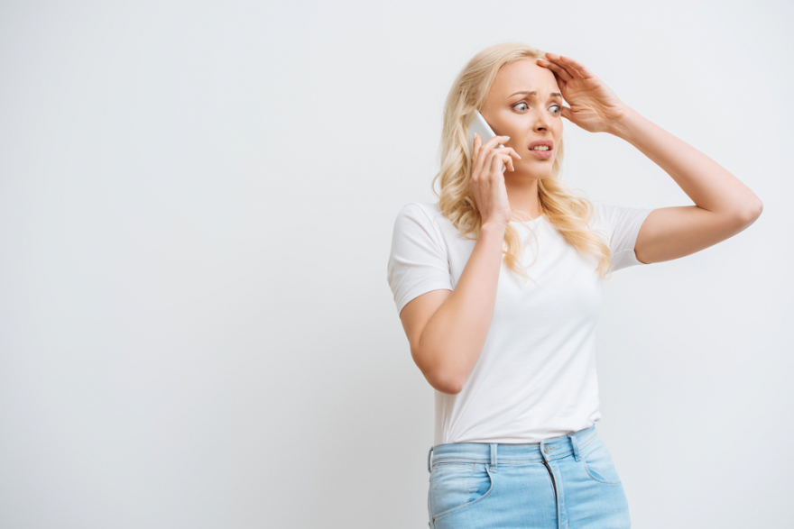 Shocked woman touching head talking on smartphone