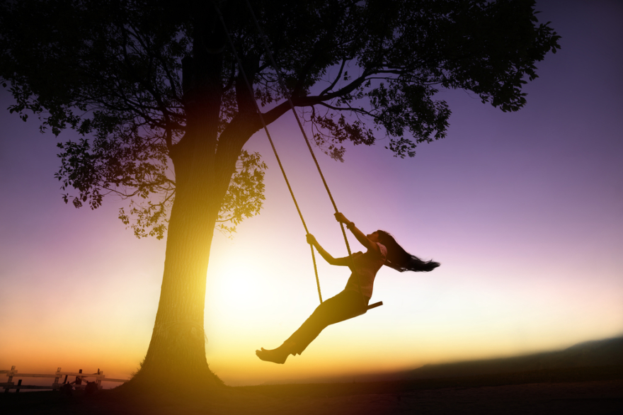 Silhouette of happy young woman on a swing with sunset background