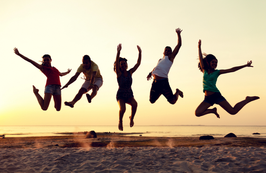 smiling friends dancing and jumping on the beach